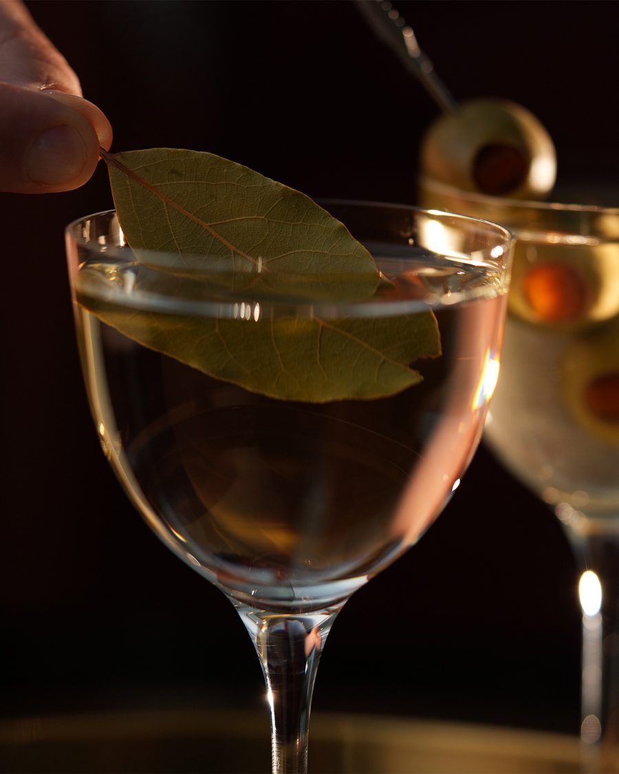 A coupe cocktail garnished with a bay leaf on a gold tray